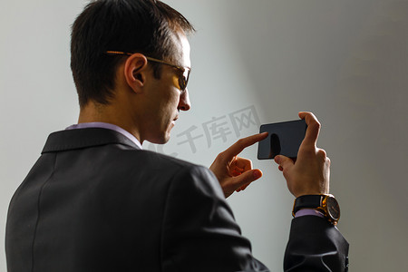 年轻开朗的黑发律师站在纯浅蓝色背景上，微笑着，穿着西装，用手机在网上阅读好消息