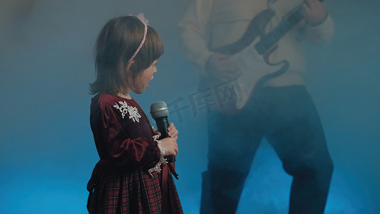 穿着复古裙子的小女孩在舞台上唱歌，她的父亲弹着电吉他