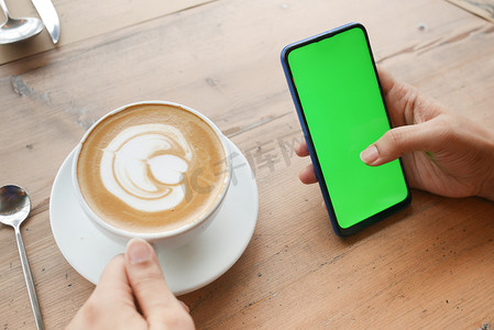 手机花屏摄影照片_拿着咖啡的CPU并使用带绿屏的智能手机