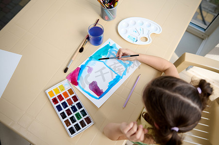 从上面看一个小女孩，有才华的孩子用画笔和水彩颜料画画