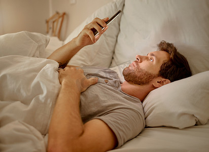 社交媒体、移动应用程序和放松男人用智能手机使用互联网或在线网站内容晚上在他的卧室与家庭无线网络。