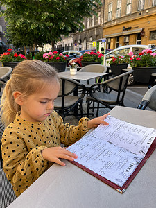 露天餐厅摄影照片_小女孩在露天餐厅的桌子上阅读菜单