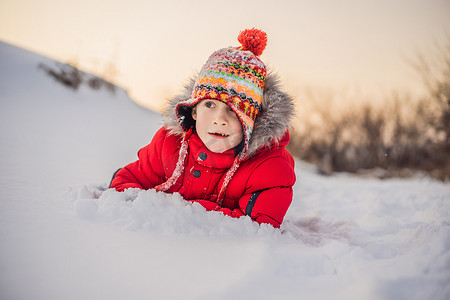 下雪玩耍摄影照片_穿着红色时装的男孩在户外玩耍。