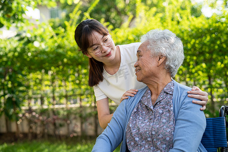坐在的摄影照片_看护者帮助和照顾亚洲老年或老年老妇人病人坐在公园的轮椅上，快乐地坐在轮椅上，健康强大的医疗理念。