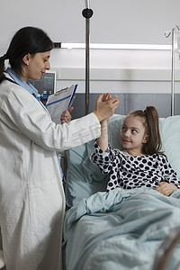 儿科专家与坐在病床上的病童做高五手势