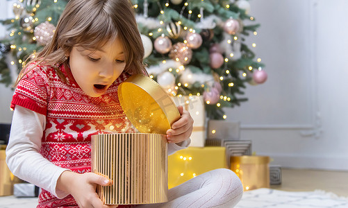装饰礼物盒摄影照片_孩子在圣诞树下打开礼物。
