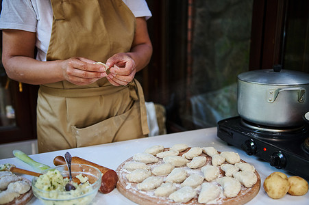 手工煮饺子摄影照片_专注于木板上的自制饺子或乌克兰瓦雷尼基，家庭主妇在乡村厨房做饭