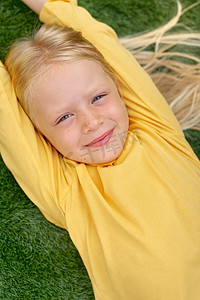 肖像可爱的金发女孩眼睛躺在，伸展在绿色的草地上。