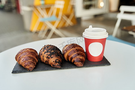 咖啡馆桌子上放着咖啡和羊角面包的红杯。