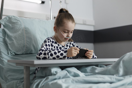 小病摄影照片_在智能手机上玩游戏时躺在床上休息的漂亮小病女孩