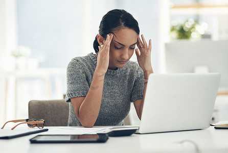 头痛、疲倦、压力大的年轻女商人坐在办公桌前，笔记本电脑上有财务问题。