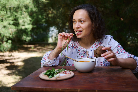 民间菜摄影照片_迷人的多民族女性吃乌克兰国菜 — 传统罗宋汤，在乡村享用午餐