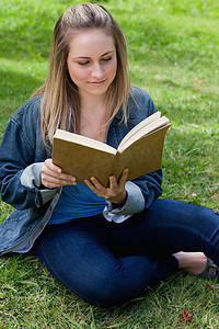盘腿坐的女孩摄影照片_年轻轻松的女孩坐在草地上看书