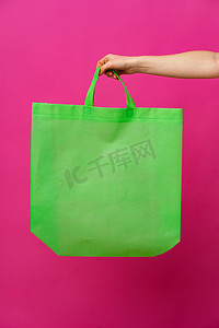 购物袋样机摄影照片_粉红色背景下女性手持生态或可重复使用的购物袋