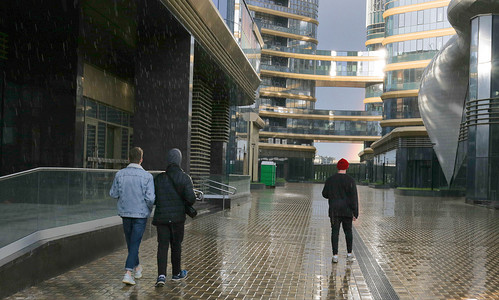照片中，三个年轻人在雨中走在城市的道路上。