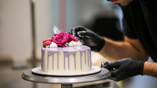 旋转的糖果摄影照片_设计师用标志装饰磨砂丁香浪漫生日快乐蛋糕顶部