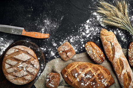 法式长棍面包、烤面包、面粉和小麦穗组合物的顶视图，深色背景上撒有小麦粉