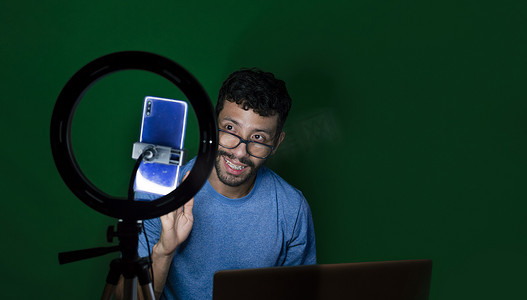 用笔记本电脑制作视频博客的年轻人，用手机制作内容的年轻人创作者，用笔记本电脑进行绿色背景视频通话的男人，