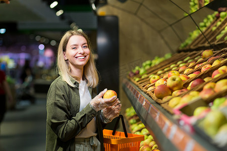 超市水果柜台摄影照片_年轻的金发女郎在超市柜台上挑选水果蔬菜。