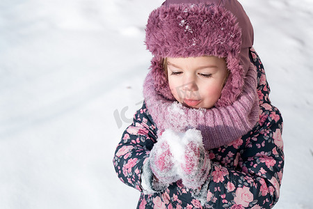 冬天、游戏、家庭、童年概念 — 穿着粉色帽子保暖衣服的正宗学龄前小女孩特写肖像，在寒冷的严寒天气里有着有趣的微笑。