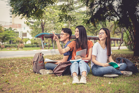 一群亚洲大学生在户外草地上读书并辅导特别班考试。