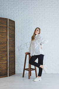 一位身穿黑裤和白衬衫的年轻女子，靠着白砖墙，一位穿着白色皮革乐福鞋的时尚现代女孩