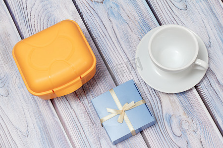 塑料黄色午餐盒、礼品和带碟子的杯子在木制背景上。