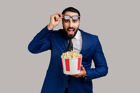 精彩运动摄影照片_男人对电影印象深刻，拿着爆米花，观看精彩的电影，举起 3D 眼镜。