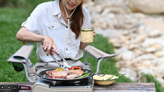 在自然公园露营时，女游客在金属炉上烤肉。