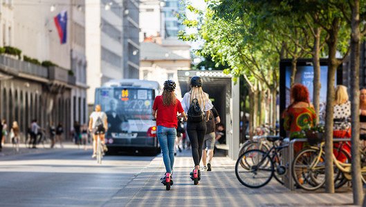 公共生活摄影照片_城市环境中时尚时尚少女骑公共租赁电动滑板车的后视图。