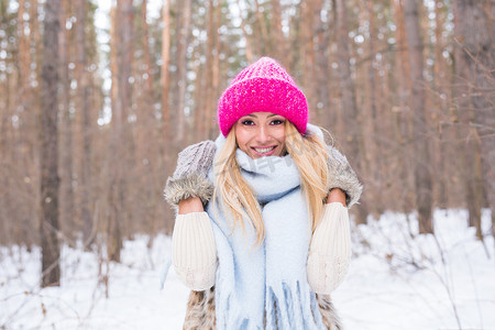 时尚与人的概念 — 在冬季雪地公园里身着白色外套和粉红色帽子的迷人金发女郎肖像
