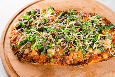 纯素 pinsa romana 配蘑菇、芦笋、玉米、豌豆、胡萝卜、奶酪和酱汁，在木板上饰有微型蔬菜。