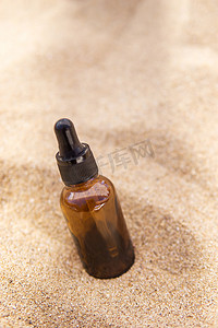 玻璃瓶中的化妆品血清，沙子中有吸管