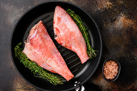 鲜海红鲈鱼，在煎铸铁锅中，在古老的深色乡村餐桌背景中，俯视平躺