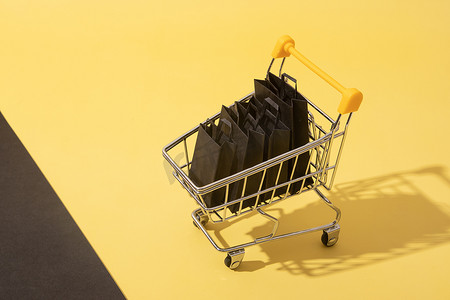 星期五黄色摄影照片_黄色背景黑色星期五销售中带购物袋的微型超市推车