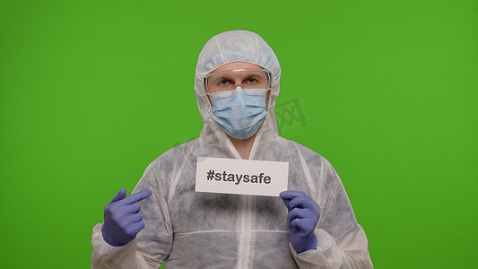色度摄影照片_身着 PPE 服的医生画像，纸上刻有文字标语，在色度键上保持安全