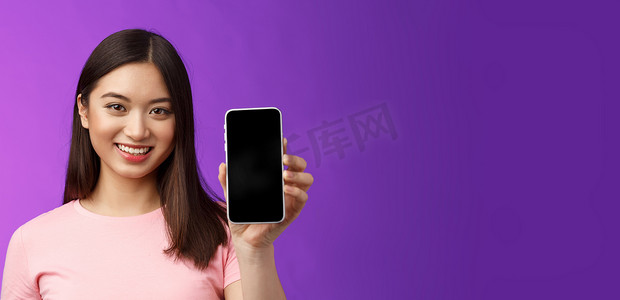 特写迷人宜人的女店员展示新的手机应用程序，手持智能手机显示电话屏幕，介绍展示的应用程序，站立紫色背景高兴