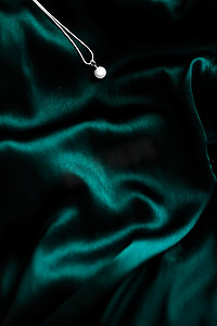 丝绸珠宝摄影照片_深翠绿色丝绸背景的豪华白金珍珠项链，节日魅力珠宝礼物