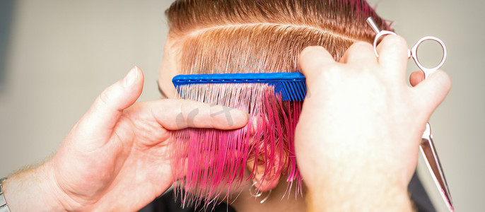 美发师的手梳理头发，为美容院的年轻白人女性制作粉色短发。