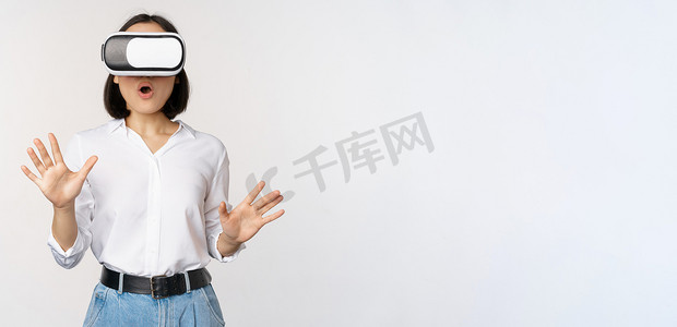 虚拟现实背景摄影照片_虚拟现实中惊讶的年轻女性，使用 VR 眼镜耳机，站在白色背景上