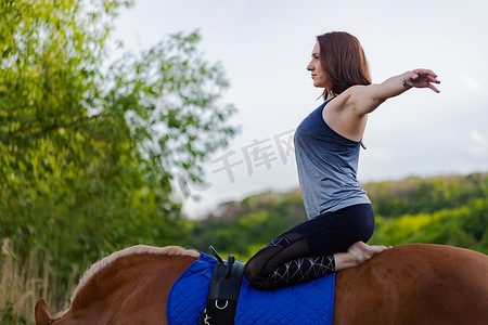 女子骑马摄影照片_在树木的背景下骑马做瑜伽的年轻女子