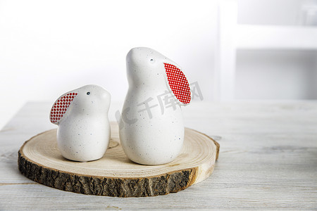 兔子圆摄影照片_在一个白色的斯堪的纳维亚风格的厨房里，两个白色野兔的小雕像，在木锯上有大大小小的红耳朵，还有一个背景是鸡蛋的碗