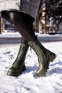 穿着绿色靴子站在雪地里的女性腿的特写镜头。