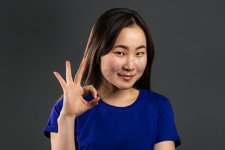 年轻的亚洲女性在灰色背景上做OK标志。