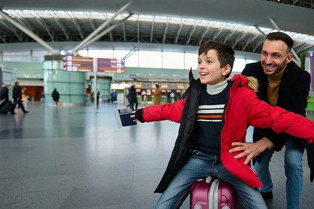 快乐的父亲和他可爱的儿子玩耍，在国际机场候机大厅等待登机时，把他放在手提箱里