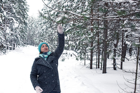 一个快乐的女人在冬天白雪覆盖的森林里，拿着一根松树枝