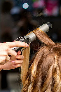 美发师在美容院用卷发器为棕色长发的年轻女子做卷发。