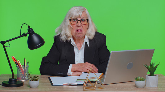 在笔记本电脑上工作的资深老办公室女商人制作滑稽面孔四处闲逛