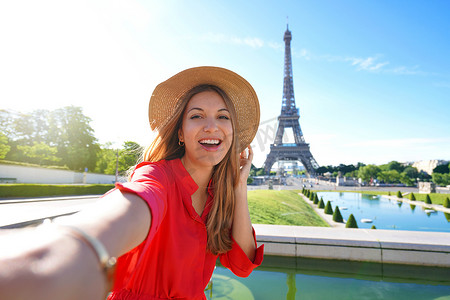 埃菲尔铁塔红色摄影照片_穿着红色连衣裙和帽子的时尚旅游女性在法国巴黎的背景下与埃菲尔铁塔合影留念。
