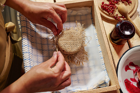 家庭主妇在粗麻布上系蝴蝶结，用自制果酱装饰罐子的盖子
